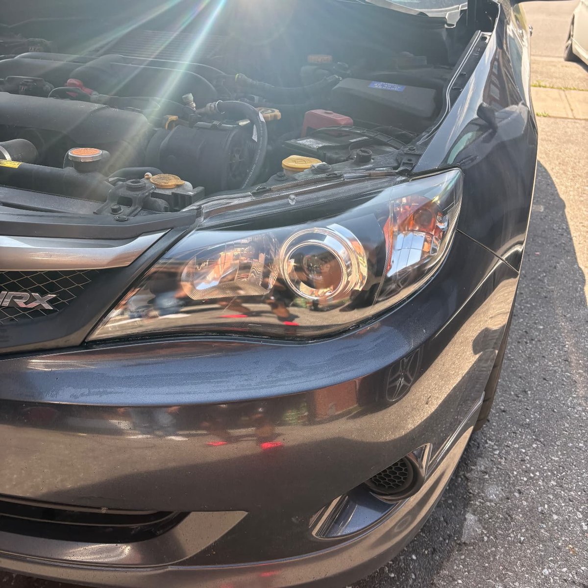 Glossy clear passenger side headlight on a grey Subaru WRX after restoration